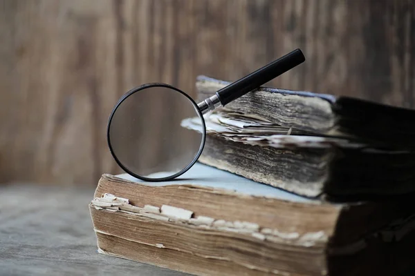 Vecchi libri su un tavolo di legno e una lente d'ingrandimento — Foto Stock