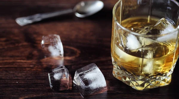 グラスに氷とウイスキー。木製テーブルの上の氷のキューブを — ストック写真