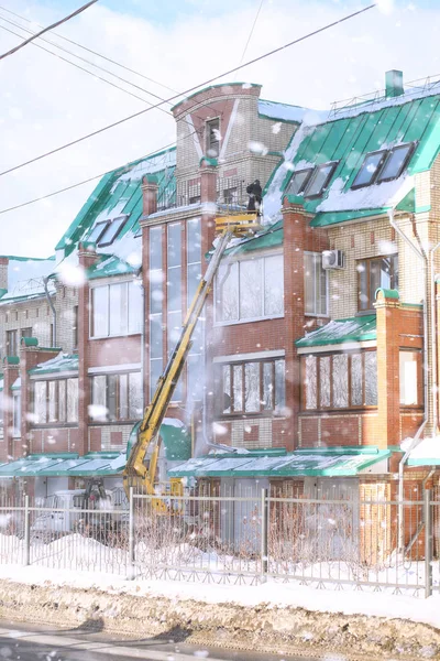 The cleaning service cleans the snow from the roof of the house.