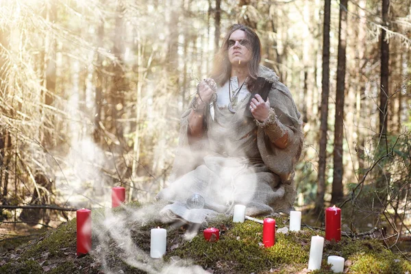 Um homem numa batina passa um ritual numa floresta escura. — Fotografia de Stock