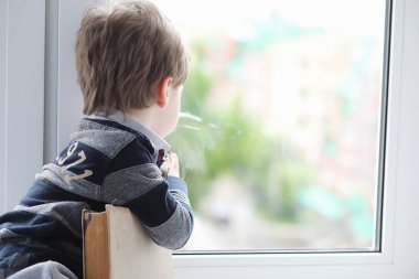 Küçük çocuk bir kitap okuyor. Çocuğun pencerenin önünde oturur bir