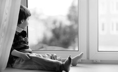 Küçük çocuk bir kitap okuyor. Çocuğun pencerenin önünde oturur bir