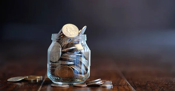 Mince ve sklenici na dřevěné podlaze. Kapesní úspory z mincí — Stock fotografie