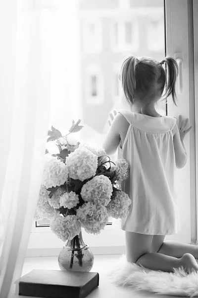 En liten flicka sitter på fönsterbrädan. En bukett blommor — Stockfoto