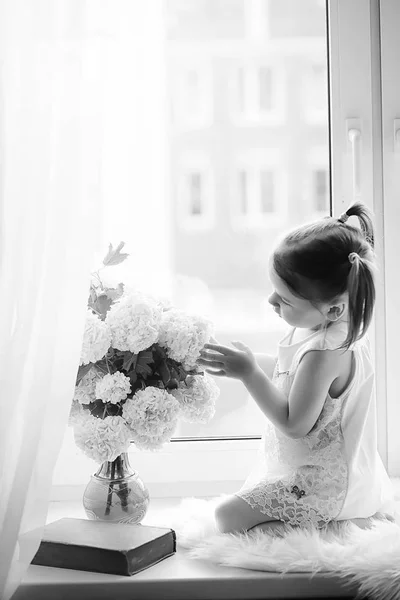 Ein kleines Mädchen sitzt auf der Fensterbank. ein Strauß Blumen — Stockfoto