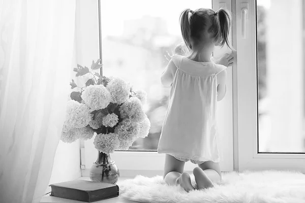 A little girl is sitting on the windowsill. A bouquet of flowers — Stock Photo, Image