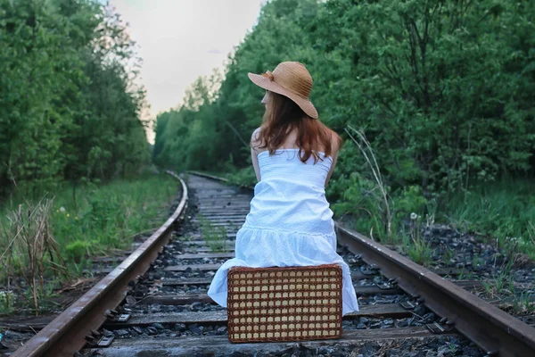 Ragazza in un sundress bianco e valigia di vimini che cammina su rotaie — Foto Stock