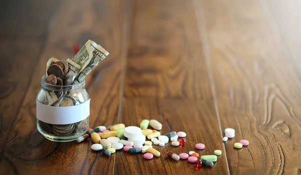 Drugs en munten in een glazen pot op een houten vloer. Zak besparingen — Stockfoto