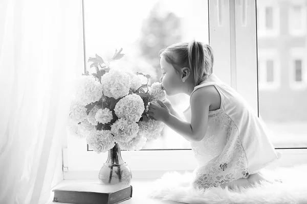 Una niña está sentada en el alféizar de la ventana. Un ramo de flores —  Fotos de Stock