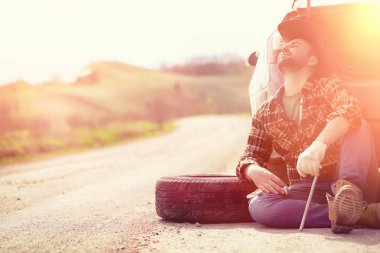 Adam yolda arabanın yanında oturuyor