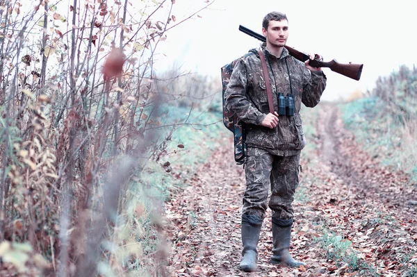 Un hombre en camuflaje y con un rifle de caza en un bosque en una sp — Foto de Stock