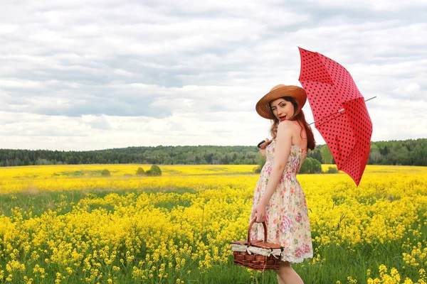 Ragazza in un campo di fiori con un ombrello e un cappello — Foto Stock