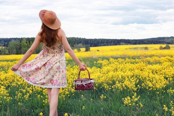 Ragazza in un campo di fiori con cesto e un cappello — Foto Stock