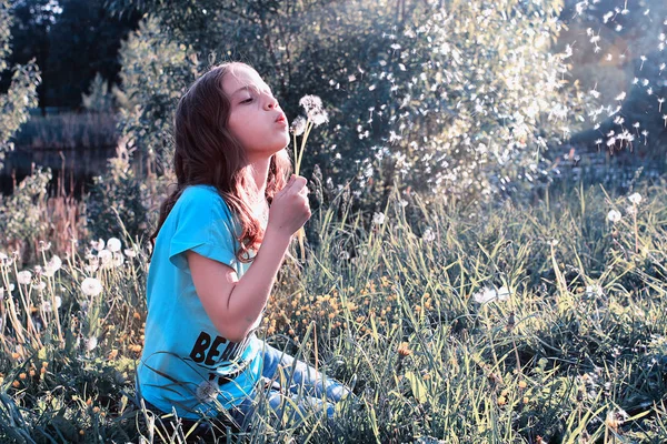 Дівчина-підліток дме насіння з квіткової кульбаби у весняному парку — стокове фото
