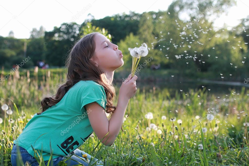 Teen blowing seeds from a dandelion flower in a spring park