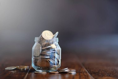 Ahşap bir zemindeki cam kavanozdaki bozuk paralar. Bozuk paradan cep tasarrufu