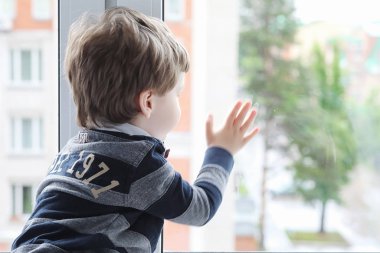 Küçük çocuk bir kitap okuyor. Çocuğun pencerenin önünde oturur bir