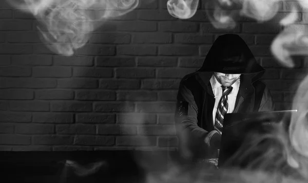 Хакер в черной маске и капюшоне за столом — стоковое фото