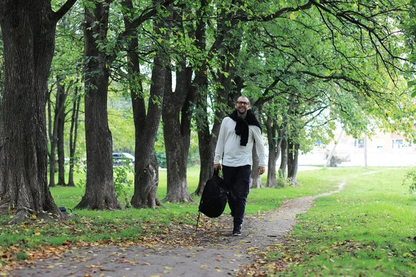 Egy szemüveges fiatalember besétál a parkba egy esernyővel. — Stock Fotó