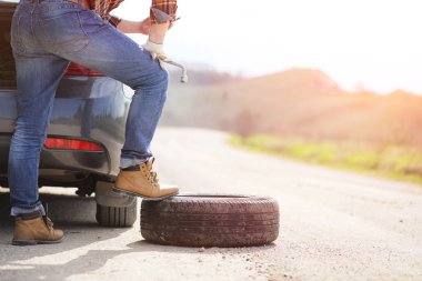 Adam yolda arabanın yanında oturuyor