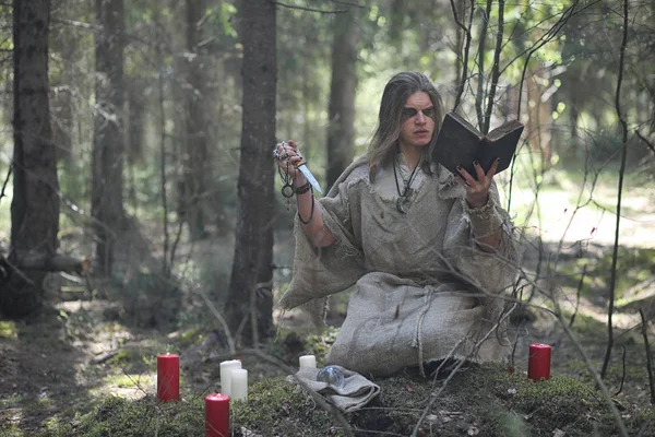 Um homem numa batina passa um ritual numa floresta escura. — Fotografia de Stock