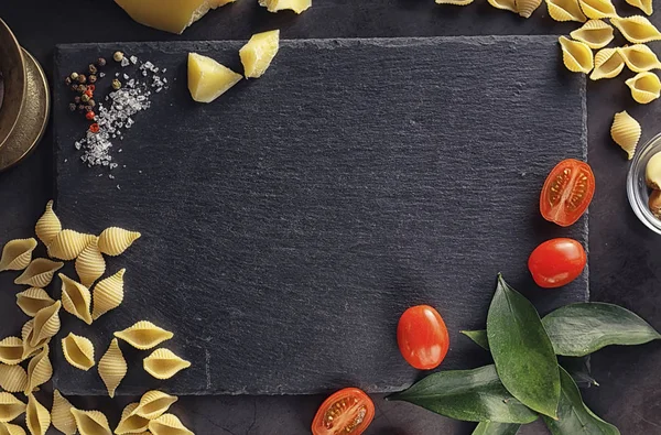 Pasta schelpen op zwarte steen. Tomaten en laurierblaadjes met allspi — Stockfoto