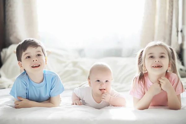 Kinderen liggen op het bed naast de pasgeboren baby, zusje. — Stockfoto