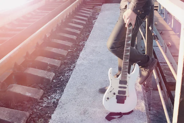 En mand med en elektrisk guitar på jernbanen. En musiker i en le - Stock-foto
