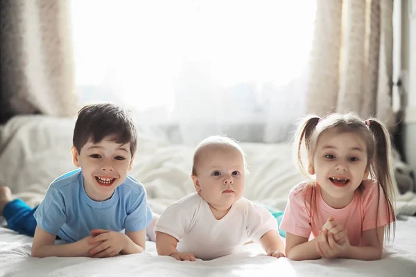 Los niños se acuestan en la cama junto al bebé recién nacido, hermanita . —  Fotos de Stock