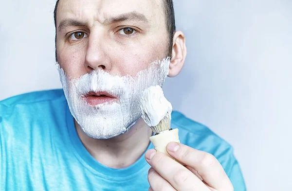 A man shaves in front a mirror. Shaving foam. Disposable razor. — Stock Photo, Image