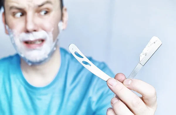 Um homem faz a barba à frente de um espelho. Espuma de barbear. Navalha descartável . — Fotografia de Stock