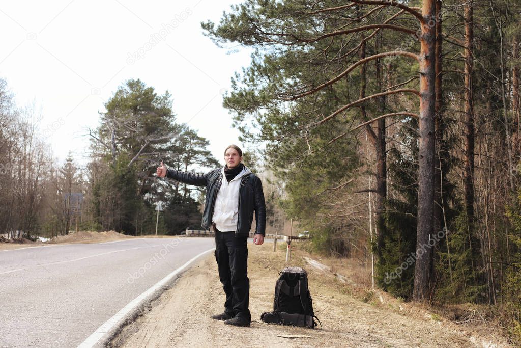 A young man is hitchhiking around the country. The man is trying