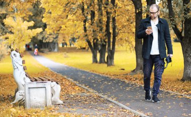 Gözlüklü genç bir adam parkta şemsiyeyle yürür.