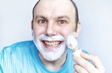 Bir adam aynanın önünde tıraş olur. Tıraş köpüğü. Tek kullanımlık jilet..