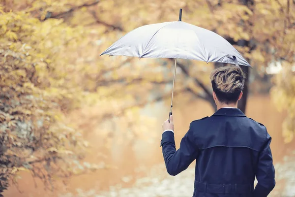 Herbstliches Regenwetter und ein junger Mann mit Regenschirm — Stockfoto