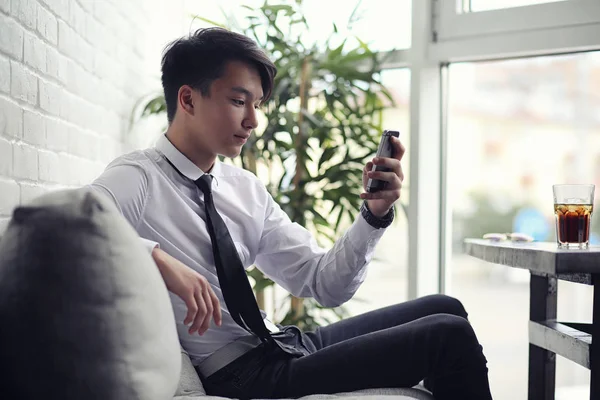 A young Asian businessman is waiting for a partner in a cafe. Bu — Stock Photo, Image
