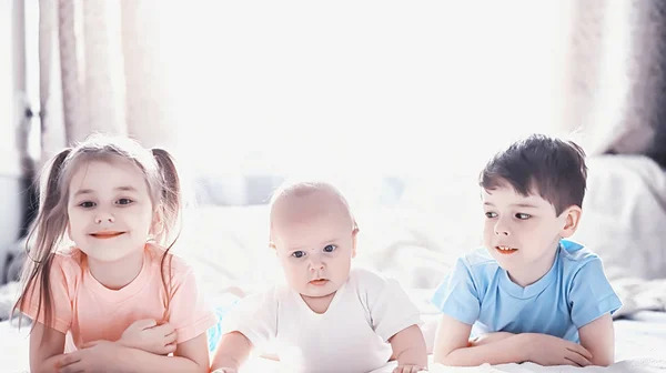 Kinderen liggen op het bed naast de pasgeboren baby, zusje. — Stockfoto