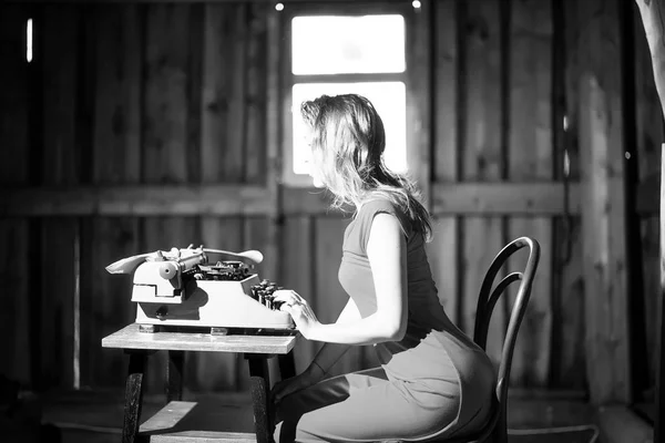 A girl prints on an old typewriter — Stock Photo, Image