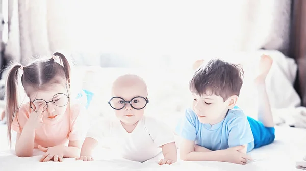 Children lie on the bed next to the newborn baby, little sister. — Stock Photo, Image