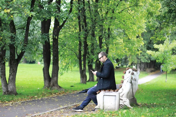 Un giovane in bicchieri cammina nel parco con un ombrello durante — Foto Stock