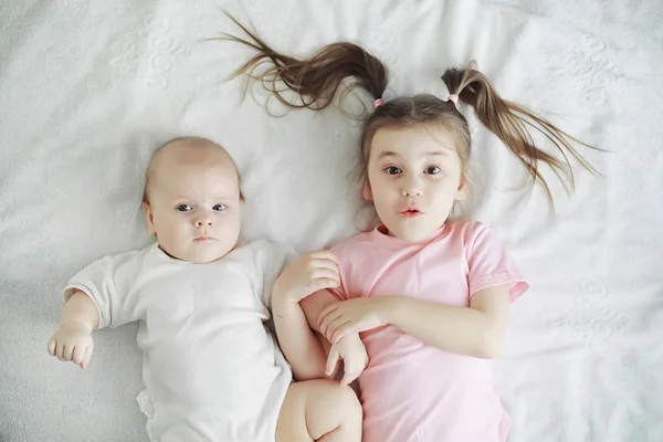 As crianças deitam-se na cama ao lado do bebé recém-nascido, irmãzinha. . — Fotografia de Stock