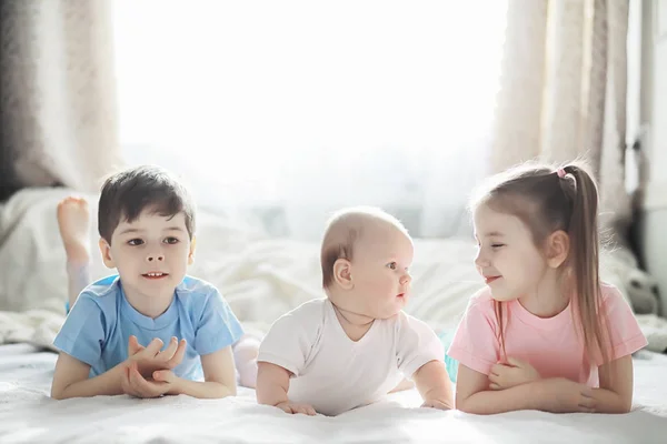 Los niños se acuestan en la cama junto al bebé recién nacido, hermanita . —  Fotos de Stock