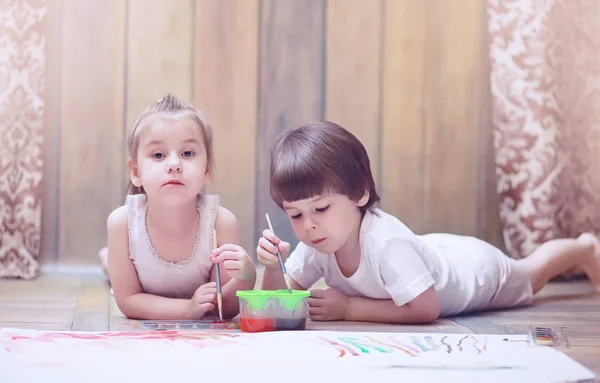 Niños pequeños pintan en una hoja grande de papel —  Fotos de Stock