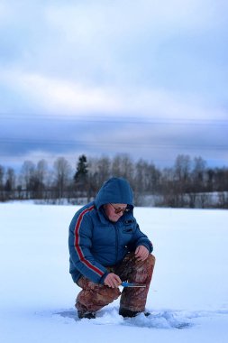 Kış mevsimi yaşlı adam gölde balık tutuyor. 