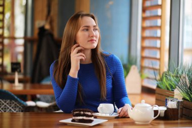 Kafede oturan ve tatlıyla çay içen genç bir kız.