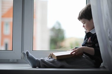 Küçük çocuk bir kitap okuyor. Çocuğun pencerenin önünde oturur ve dersler için hazırlar. Bir çocuk pencere üzerinde elinde bir kitapla