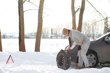 Soğuk bir kış gününde, bozuk bir arabanın yanında bir adam.