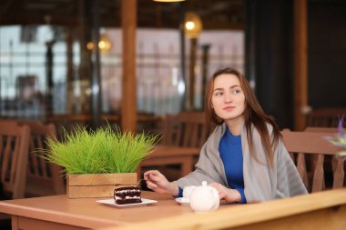 Kafede oturan ve tatlıyla çay içen genç bir kız.