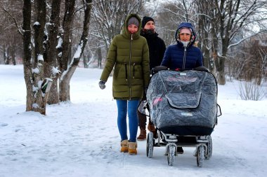 Bebek arabalı arkadaşlar, karlı kış parkında yürüyorlar.