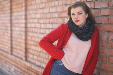 Tuğla duvarda kırmızı ceketli şirin bir kız.